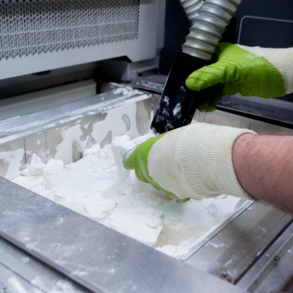 Worker taking out models of white polyamide powder and cleaning them. 3D printer